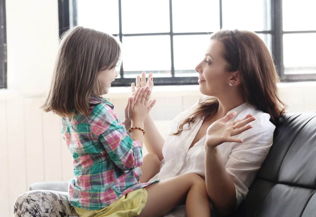 Mother sitting on the couch, with her daughter in her lap, engaging in interactive play with their hands