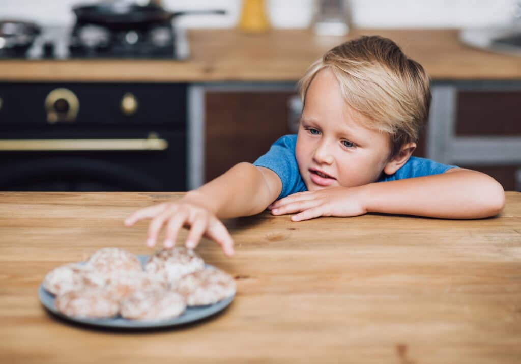 The importance of saying no to your child -Young boy reaching for a plate of tempting cookies on a kitchen counter, displaying curiosity and excitement.