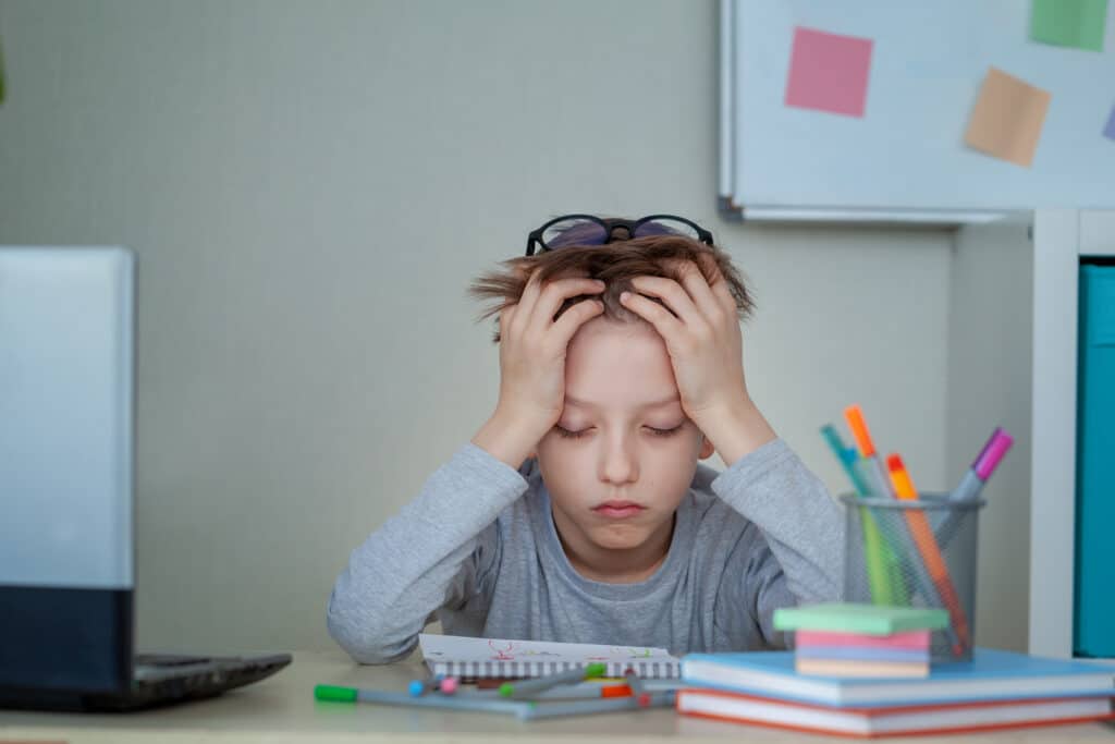 A frustrated boy with his head in his hands, eyes closed, while working on his homework.