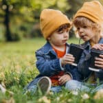 Two little brothers sitting on the grass, happily sharing cups of hot chocolate.