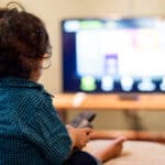 Young boy sitting alone in front of a television captivated by the content on the screen.