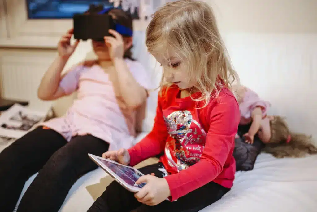 Two girls playing video games one on the tablet and the other one with virtual reality glasses