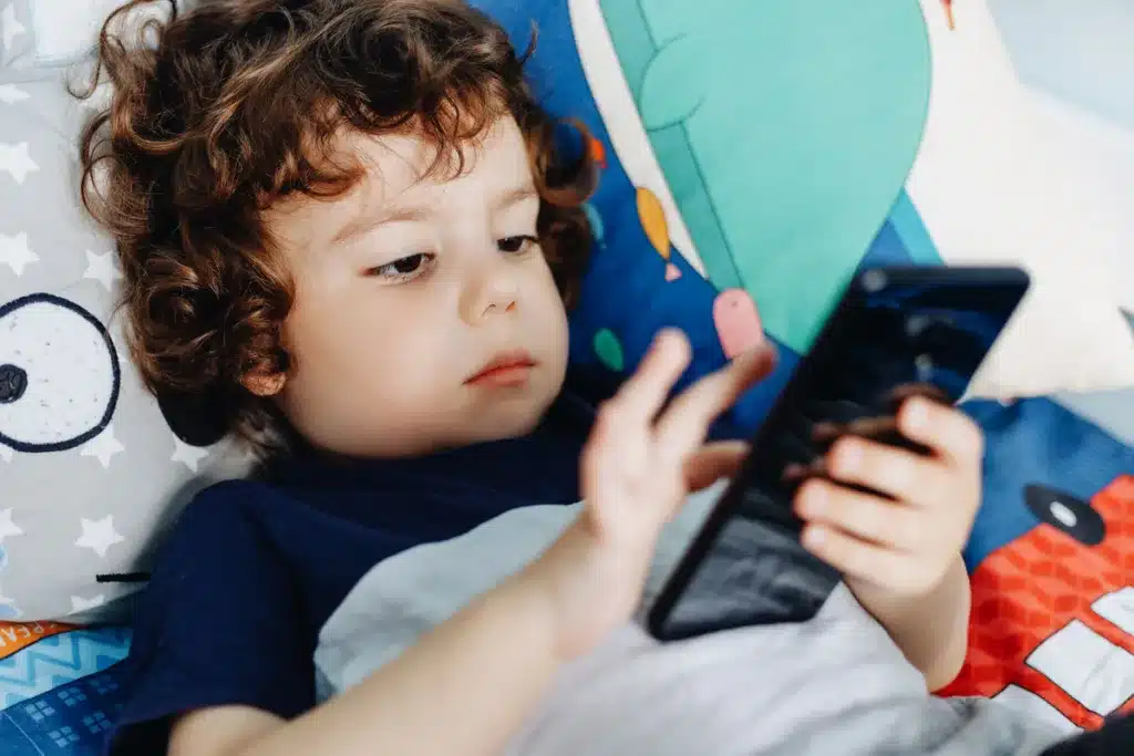 Little boy scrolling on a smartphone while in bed